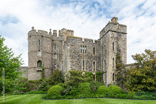 Medieval stone castle with towers and arched windows, surrounded by lush green gardens under a partly cloudy sky. Historic architecture and peaceful atmosphere.