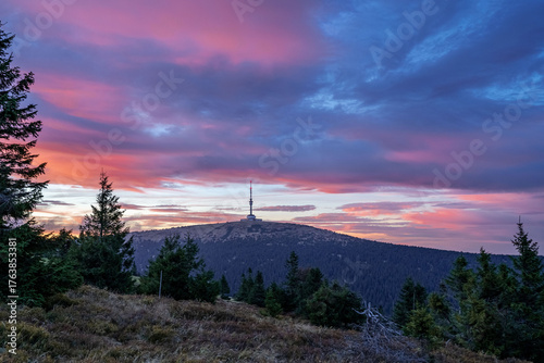 Colorful sunset over Praděd mountain in Jeseníky, Czech Republic, with the iconic TV tower on the summit and dramatic clouds above forested hills.