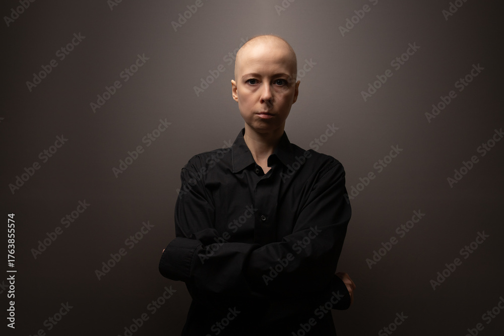 Fototapeta premium Bald woman with cancer wearing a black shirt, standing against a neutral background, symbol of strength, awareness, and recovery after chemotherapy.