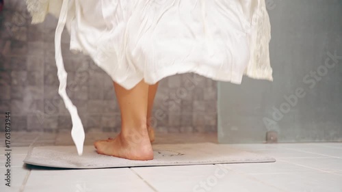 Woman Walking into Shower While White Dress Falls to Tile Floor, Rear View with Bare Legs Visible, Intimate Hygiene Concept