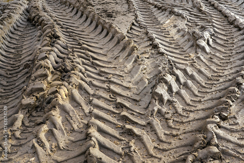 Deep tire tracks in wet muddy ground showing pattern texture from heavy construction vehicle wheels