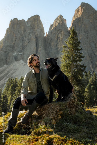 Young man posing with his black dog with Dolomites mountains views in the background