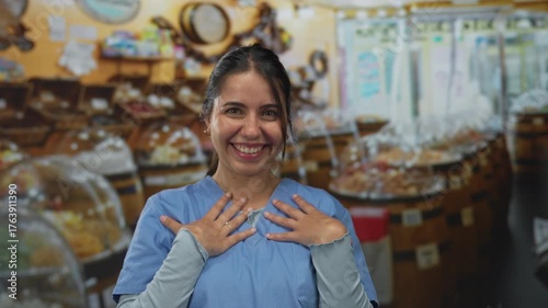 Woman smiling in a vibrant sweet shop setting, expressing joy amidst colorful candy displays indoors, wearing casual outfit, suggesting approachable personality and friendly atmosphere.