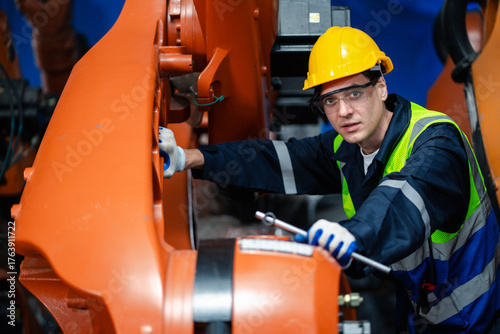 Two factory engineers wearing safety gear checking documents in front of robotic arms. Concept of teamwork, industrial automation, robotics, manufacturing process, and workplace safety.