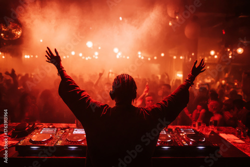 The dj stands in front of the crowd with his hands raised in the club.