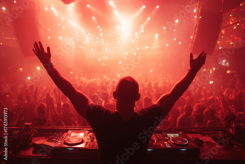 The dj stands in front of the crowd with his hands raised in the club.