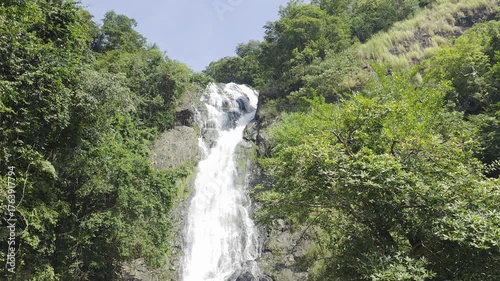 Majestic Waterfall Flowing Through Lush Green Forest Under Bright Clear Sky