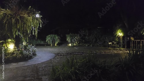 Serene Night Garden with Soft Glow from Lamps Illuminates Lush Greenery and Pathway