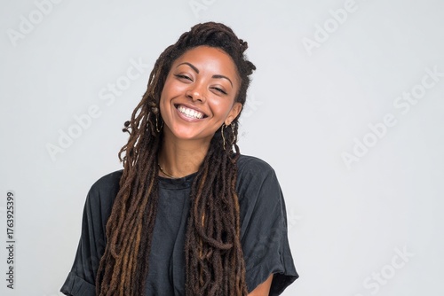 Smiling Woman With Long Dreadlocks Poses Against a Light Background in a Casu...
