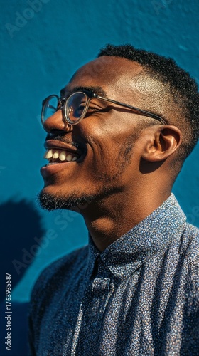Smiling Man With Glasses Standing Against a Blue Wall in Bright Sunlight