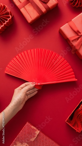 Red Fan Held by a Hand Surrounded by Red Gifts on a Festive Table