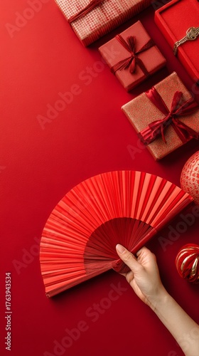 Red Fan Held by a Hand Surrounded by Red Gifts on a Festive Table