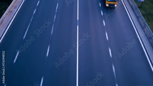 Four semi trucks two yellow and two blue drive on a highway with white lane markings the trucks are in motion and the background is blurred suggesting speed and transit on the road