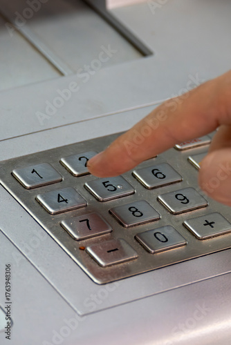 Fotografie A person who uses their hand to enter their card PIN to withdraw money from an ATM