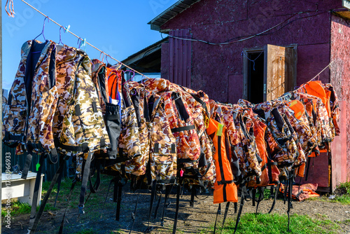 Colorful life jackets drying in the sun near a rustic building by the water at midday