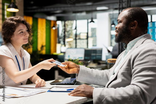 Fotografi Interviewer handing workplace badge to new hire after the recruiting process, completing registration with ID confirmation on credentials for the role within the corporate office system