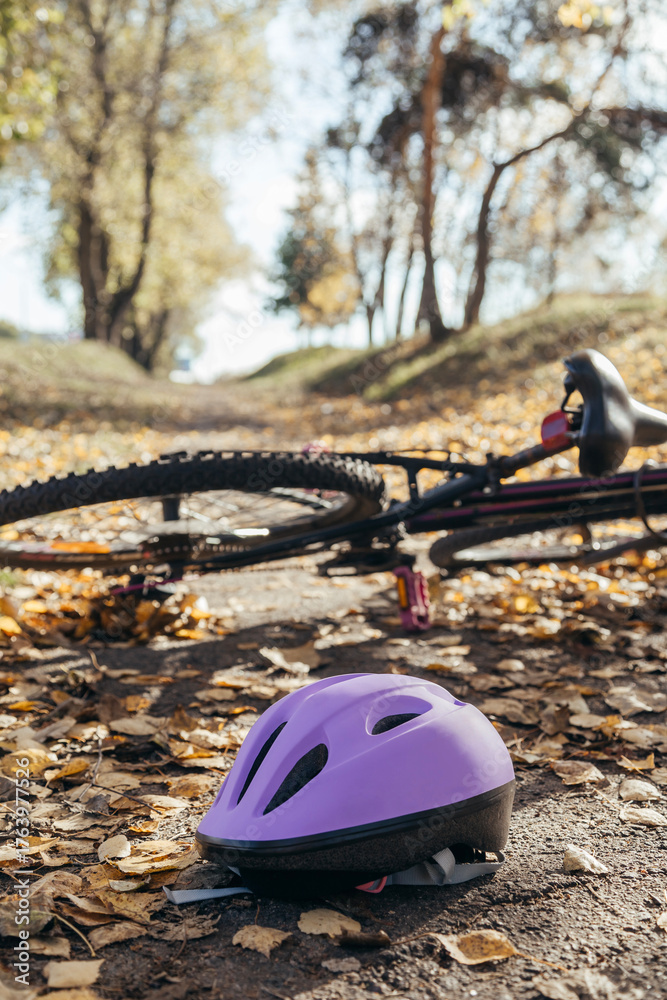 Naklejka premium Purple helmet lies abandoned on the pavement beside a toppled bicycle, evidence of a sudden fall.