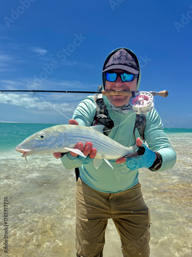 Fly fisherman holding a freshly caught bonefish while standing on the crystal-clear tropical flats of Kiritimati (Christmas Island), Kiribati. This remote Pacific atoll is internationally recognized a