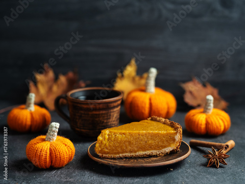 A slice of traditional pumpkin pie and a cup of coffee on a table with small crocheted pumpkins, copy space
