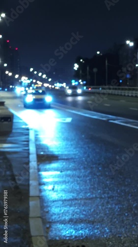 Night city road with car headlights and reflections on wet asphalt, urban traffic and moody blue light atmosphere
