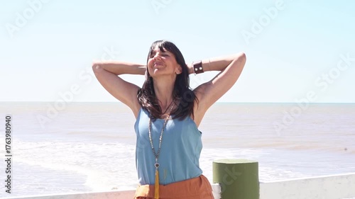 Woman with open arms embracing the ocean wind and sunshine on a pier.