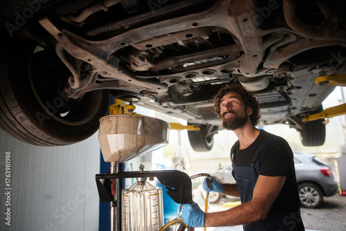 Fotografie A skilled car mechanic is working under a vehicle in a garage, conducting an oil change while ensuring precision and safety