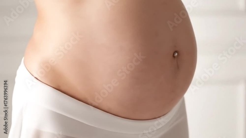 Pregnant Woman Belly with Navel Ring and White Fabric on a White Background