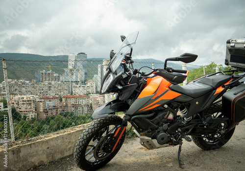 A view of a black and orange recreational motorcycle with saddlebags. Its various components and mechanisms are visible. A view of the entire motorcycle. Day.