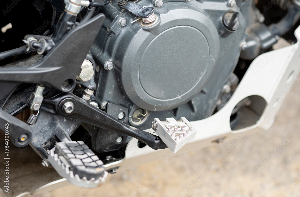 Fototapeta premium A daytime view of a black and orange recreational motorcycle with saddlebags. Its various components and mechanisms are visible. A view of the right engine cover, footrest, and rear brake lever.