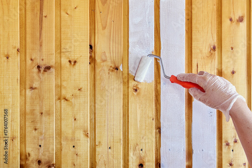 Painting wooden paneling white color house painter uses small paint roller dipping paint in tray.