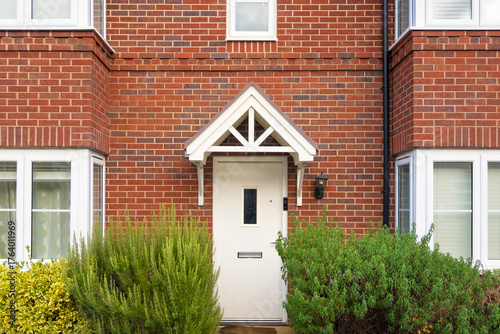 Red brick family house in UK - Real estate and housing concepts. White front door in traditional new neighbourhood at the suburbs of English town. Street with semi-detached, detached, terraced house.