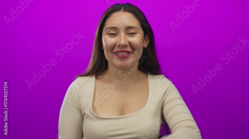 Woman with pink soft lips and raised hand blows kiss gesture in purple studio; affection longing desire.