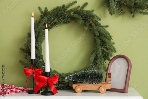 Burning candles with Christmas wreath and decor on fireplace near green wall
