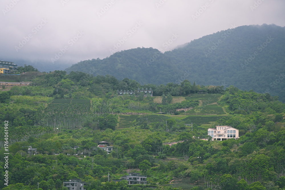 Fototapeta premium Layered green mountains with terraced rows and buildings, misty peaks in background viewed from Pobuwo area across Lanyang River, Sanxing, Yilan County, Taiwan.