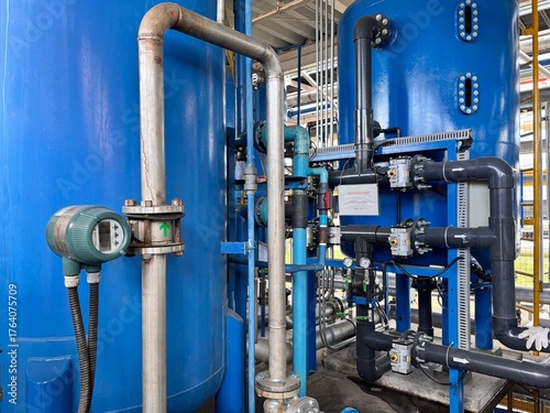 Industrial water treatment plant equipment, featuring blue tanks, pipes, and a flow meter, essential for purification and process control.