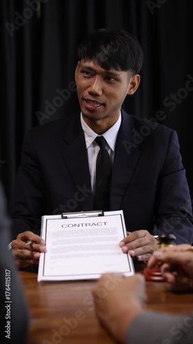 Professional lawyers negotiating contract details, sitting at wooden table while reviewing and signing legal document in formal office.