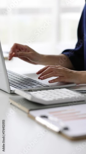 Professional female accountant analyzing financial data using laptop and calculator, carefully reviewing reports.