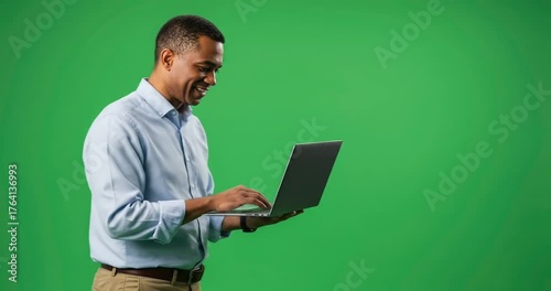 Smiling man using laptop against green screen backdrop in studio.