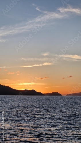 Stunning sunset reflecting on the tranquil ocean with distant islands creating a peaceful tropical vibe, perfect for travel blogs or serene backgrounds
