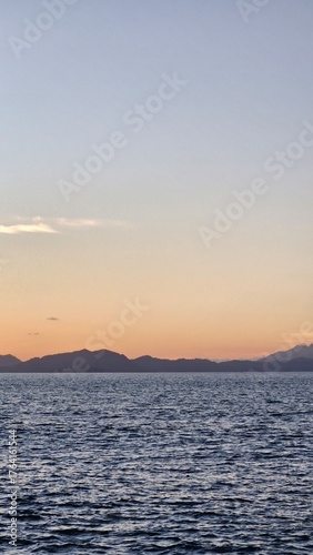 Serene ocean view at sunset with distant mountains creating a tranquil, peaceful scene perfect for travel or relaxation themed projects and creative content