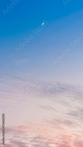 Serene crescent moon shines in the tranquil blue sky above soft pastel clouds at twilight, perfect for peaceful backgrounds and atmospheric designs