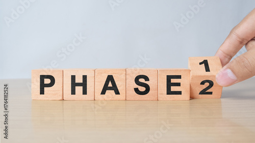Time for Phase 2. Hand is turning a cube and changes the word 'Phase 1' to 'Phase 2'. Beautiful white background. Business concept