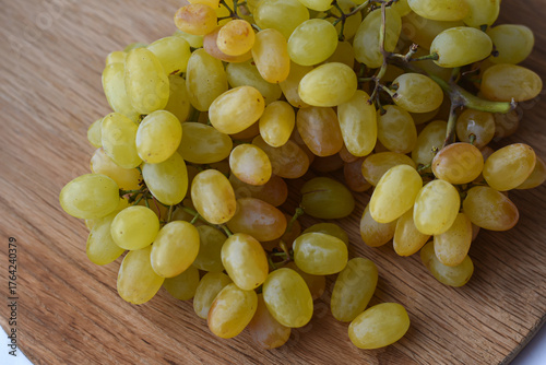 Large bunch yellow grapes on wooden plate. Food and summer background. Ripe grape Kishmish, sultana on wooden circle surface.