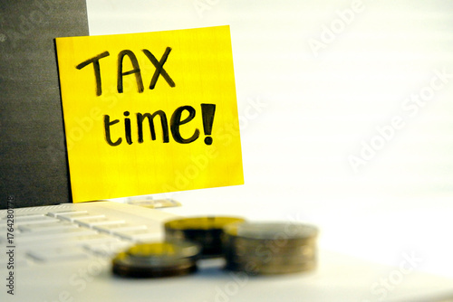 Tax Season: tax time reminder background digitally generated image stock photo copy space yellow note pad vertically stick on the note book coins stacks foreground