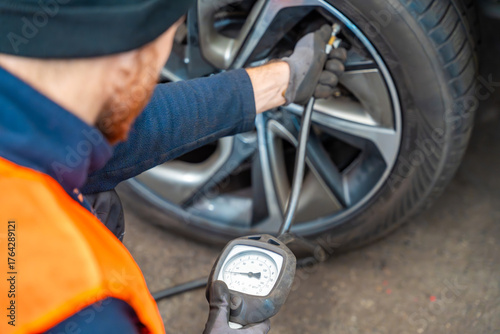 Worker checking tire pressure with gauge after seasonal wheel replacement. Final step of winter tire preparation in auto service in Czech Republic.