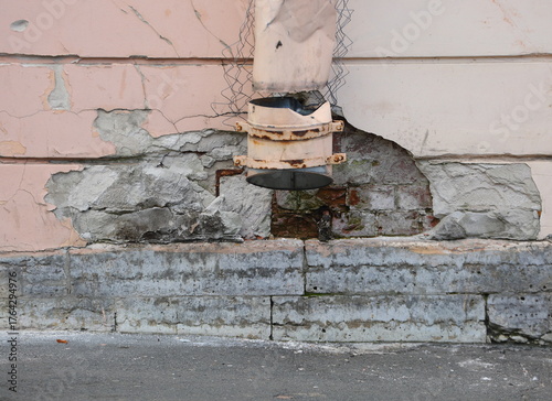 A broken drainpipe on a wall with crumbling plaster