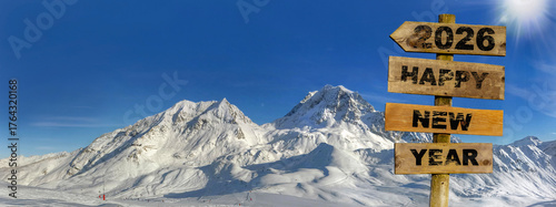 happy new year 2026 written on a wooden directional sign with a panoramic view of the snowy peaks of a ski area in the Alps background
