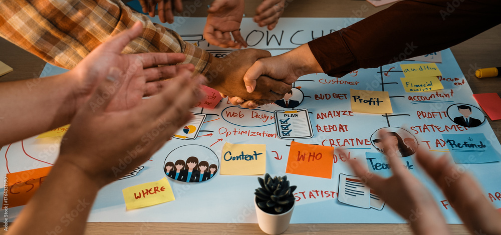 Obraz premium A dynamic scene of hands shaking above a table filled with notes and diagrams highlights teamwork in business strategy development. The atmosphere promotes collaboration and creativity. SACTR