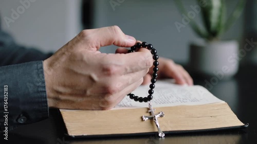 Man holding rosary with crucifix over open Bible on table