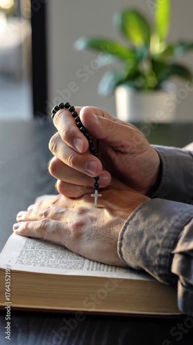 Man holding rosary with crucifix over open Bible on table, vertical footage